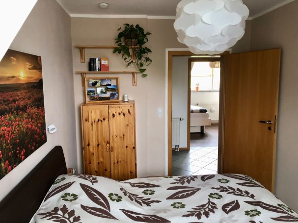 Helles Schlafzimmer mit Holzmöbeln, Blumenkunst und Zugang zu einem Bad.