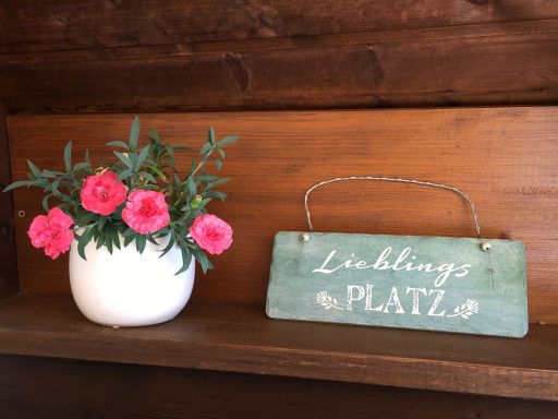 Blumen in einem weißen Topf und ein Holzschild mit der Aufschrift "Lieblingsplatz".