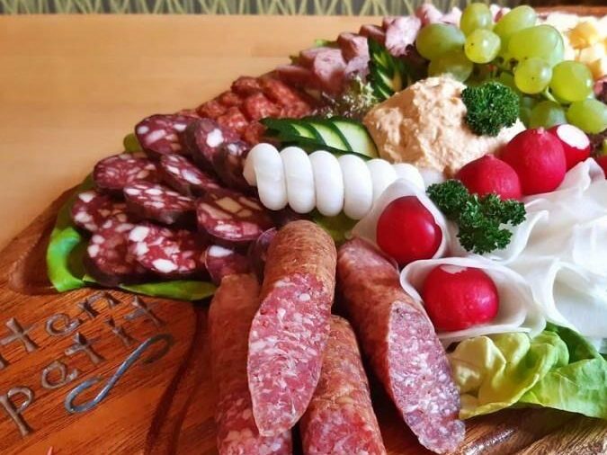 Ein rustikales Plattenarrangement mit Wurst, Käse, Oliven, Trauben und frischem Gemüse.