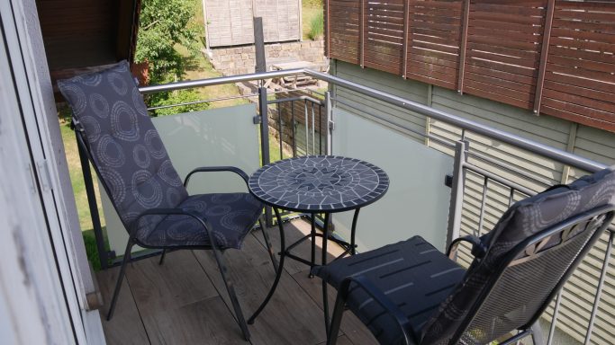 Balkon mit zwei Stühlen und einem runden Tisch, umgeben von Pflanzen.