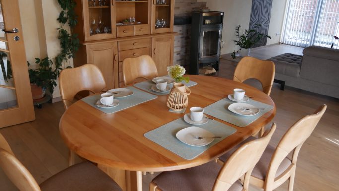 Runder Tisch mit gedecktem Frühstück, Stühlen und Holzschränken im Hintergrund.