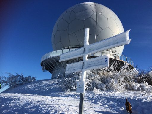 Wegweiser im Schnee vor einer großen, runden Radaranlage.