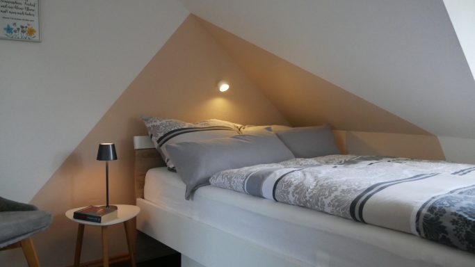 Gemütliches Schlafzimmer mit einem Bett, Nachttisch und Fenster im Dachgeschoss.