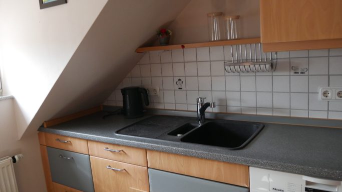 Küche mit schräger Decke, Spüle, Küchenzeile und Küchengeräten.