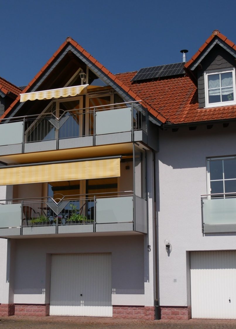 Helles Wohnhaus mit Balkon, gelber Markise und modernen Fenstern.
