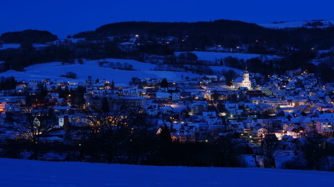 Dorf bei Nacht mit beleuchteten Häusern und schneebedeckten Landschaften.