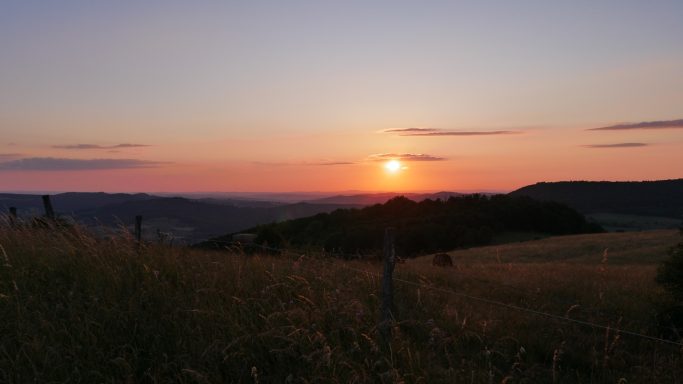 Sonnenuntergang über einer hügeligen Landschaft mit grünem Gras.