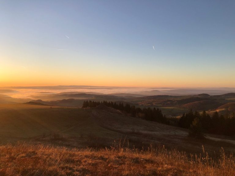 Sonnenaufgang über einer nebligen Landschaft mit sanften Hügeln.