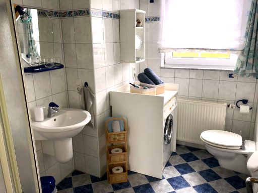 Badezimmer mit Waschbecken, Waschmaschine, WC und blauen Fliesen.